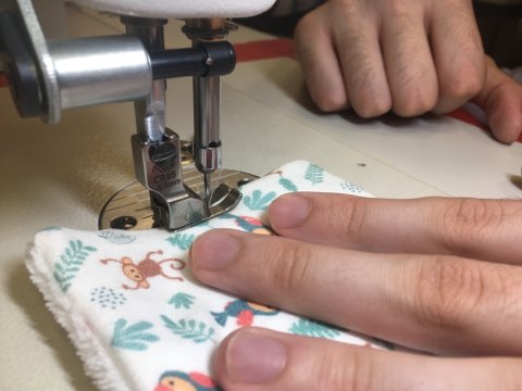 Mains d'une couturière en train de confectionner une lingette lavable avec sa machine à coudre.