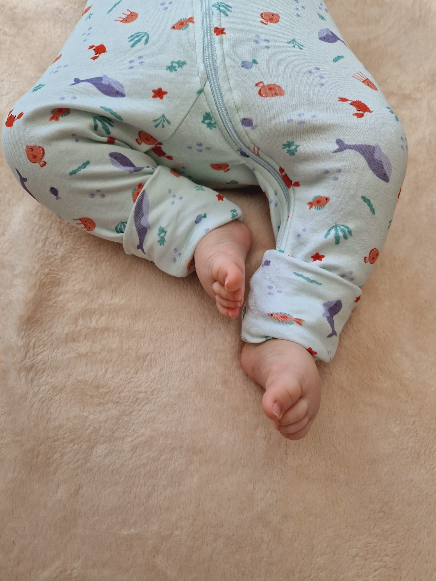 Focus sur la partie bas du corps du bébé présentant les pieds à l'air avec les chaussettes retroussables ouvertes.