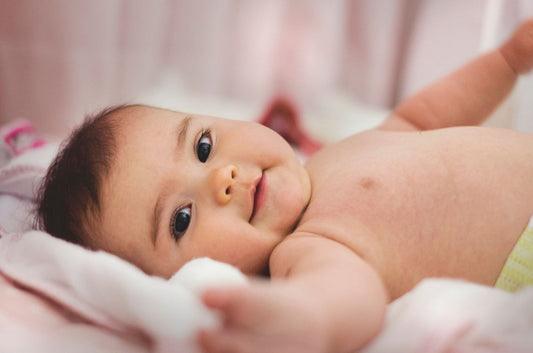 Bébé allongé sur son lit, yeux ouverts et souriant.