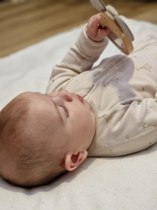 Bébé habillé avec son pyjama zippé et évolutif et qui joue avec son hochet