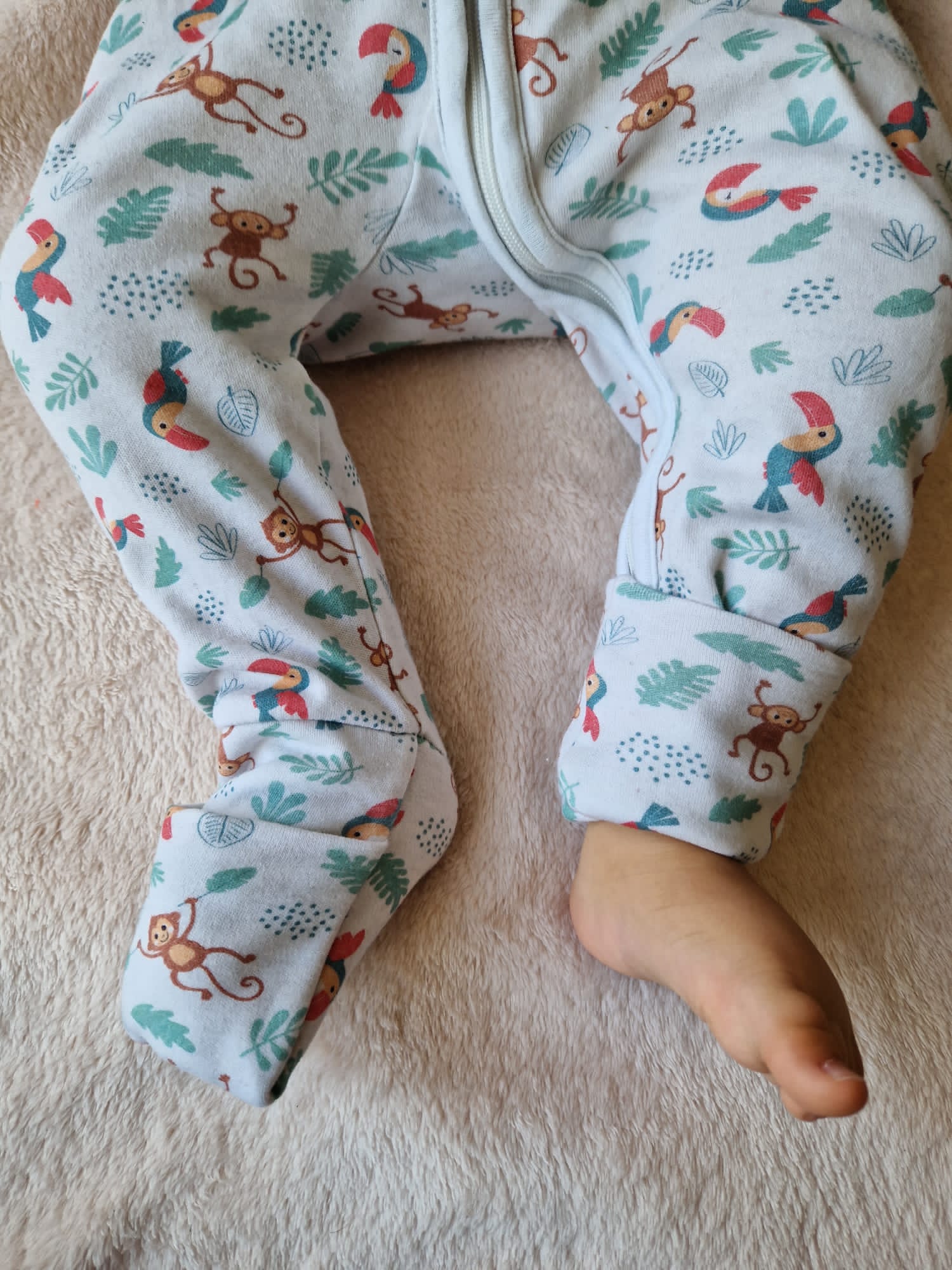 Focus sur les pieds de bébé portant le pyjama. Démonstration des chaussettes retroussables: un pied à l'air libre montrant la chaussette retroussée et un autre pied au chaud montrant la chaussette fermée.