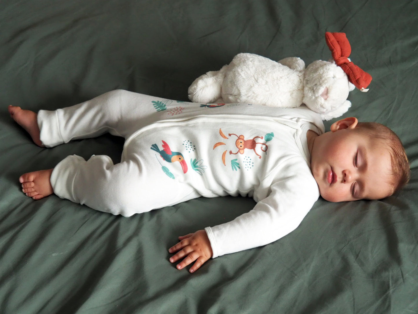Bébé qui dort sur son lit avec le pyjama de la collection jungle.