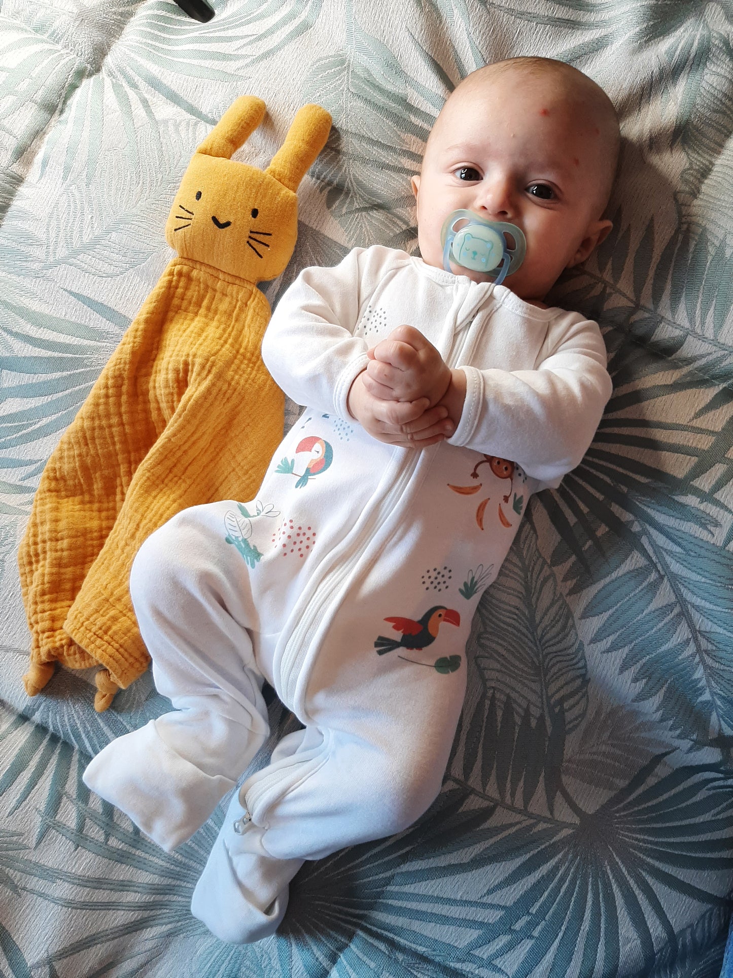 Bébé portant le pyjama "pétillant comme un toucan" de la collection Jungle avec présence de son doudou à côté.